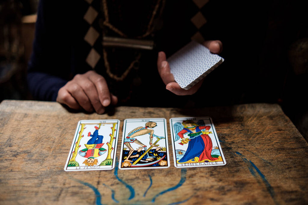 Close up os psychic reader cards on a wood table. We can see three tarot cards and the hand of the reader. - Foto, Bild