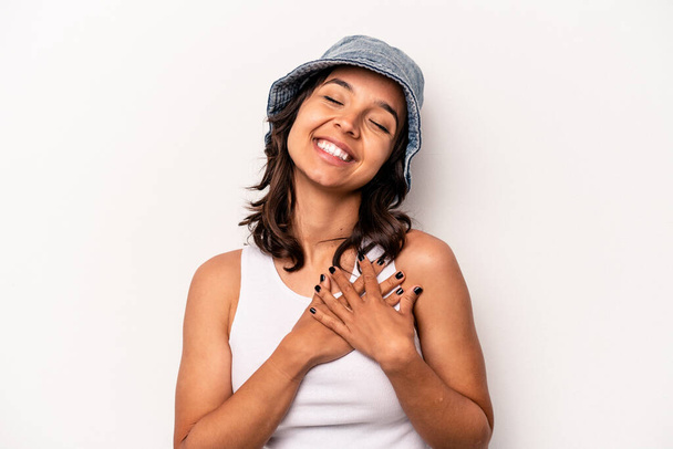 Jeune femme hispanique isolée sur fond blanc riant en gardant la main sur le cœur, concept de bonheur. - Photo, image