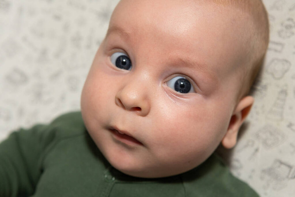 крупным планом портрет трехмесячного ребенка с голубыми глазами, одетым в зеленый цвет - Фото, изображение