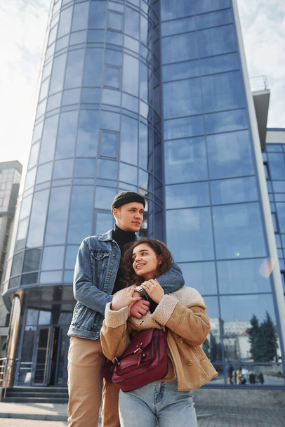 Cheerful couple in casual warm clothes have a walk outdoors in the city near business building. - Zdjęcie, obraz