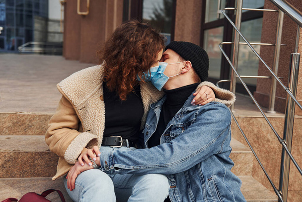 Couple in protective masks kissing each other in the city near business building at quarantine time. Conception of coronavirus. - Foto, Bild