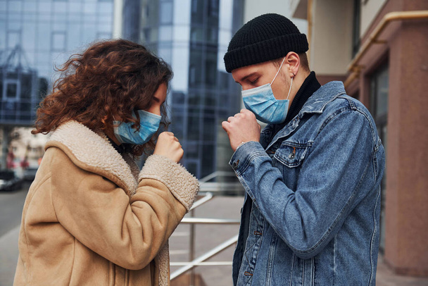 Couple in protective masks have a cough outdoors in the city near business building at quarantine time. Conception of coronavirus. - Φωτογραφία, εικόνα