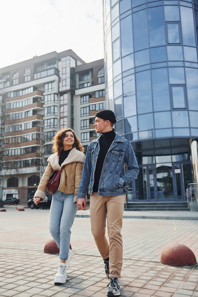 Cheerful couple in casual warm clothes have a walk outdoors in the city near business building. - Foto, Imagen