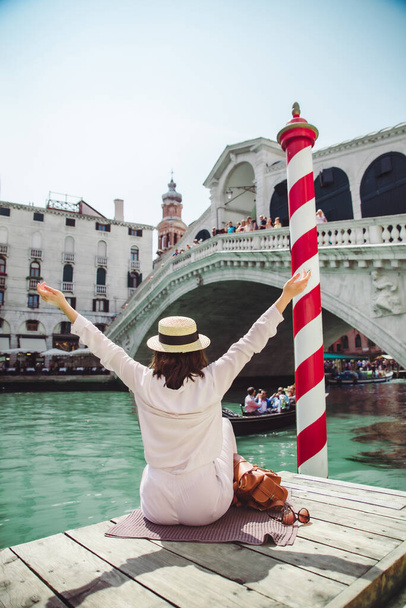 vrouw zit in de buurt van Rialto brug in Venetië italië op zoek naar een groot kanaal met gondels zomer tijd kopiëren ruimte - Foto, afbeelding