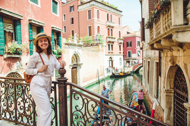 young pretty woman traveler standing at venice bridge cross canal gondolas in water - Photo, Image