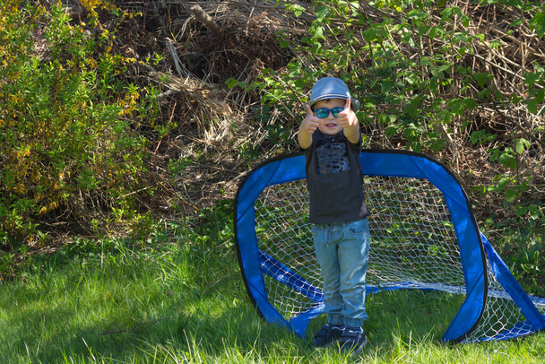 Kisfiú kalapban és napszemüvegben focizás közben a kertben - Fotó, kép