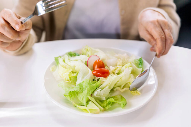 Close up a fresh and clean vegetarian salad (lettuce, tomato and sliced radish) served for senior woman patient at home. Caregiver visit at home. Home health care and nursing home concept. - Foto, imagen