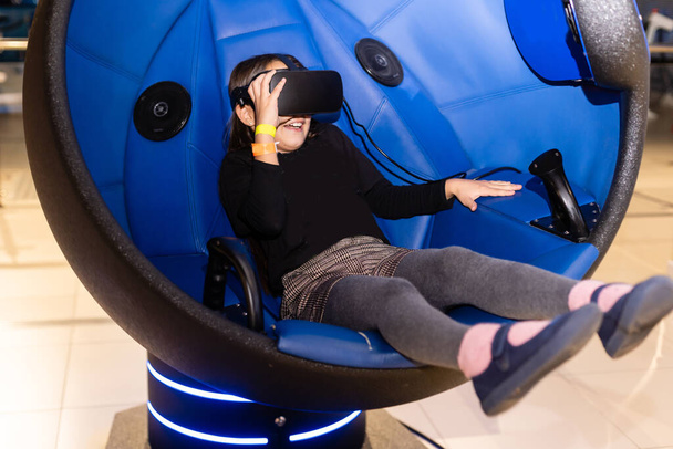 Een klein meisje zit in een gaming cockpit en houdt het race stuurwiel om een race simulatie te spelen - Foto, afbeelding
