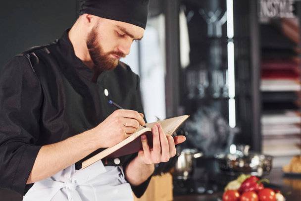 Professional young chef cook in uniform standing with notepad on the kitchen. - Foto, Bild