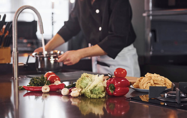 Apparatuur gebruiken. Professionele jonge chef-kok koken in uniform werken aan de keuken met groenten. - Foto, afbeelding