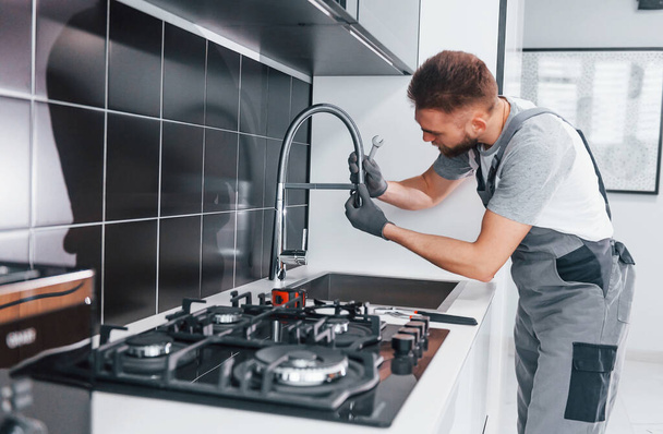 Young professional plumber in grey uniform fixing water tap on the kitchen. - Foto, immagini