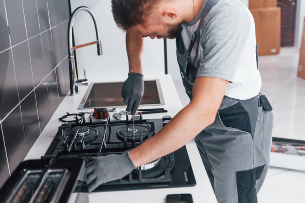 Young professional plumber in grey uniform working on the kitchen. - Фото, зображення