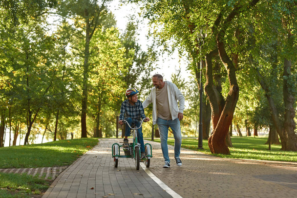 Joyful father walk and help son ride tricycle - 写真・画像