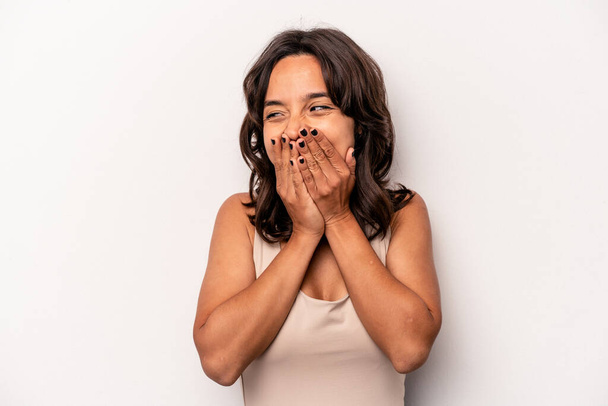 Jeune femme hispanique isolée sur fond blanc riant de quelque chose, couvrant la bouche avec les mains. - Photo, image