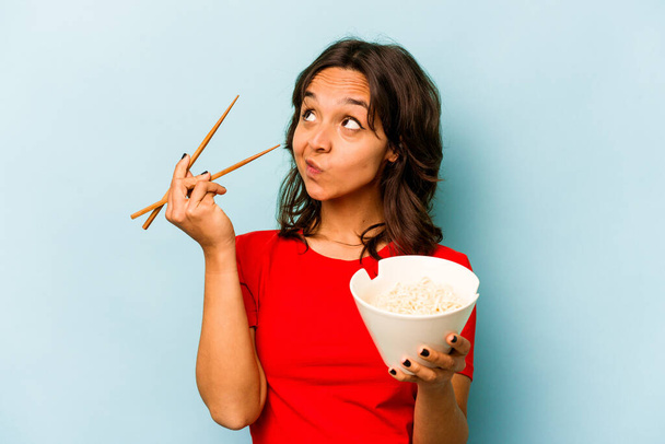 Young hispanic woman eating noodles isolated on blue background - Zdjęcie, obraz