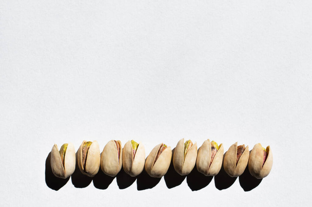 vista plana de la fila con pistachos salados agrietados sobre fondo blanco - Foto, Imagen