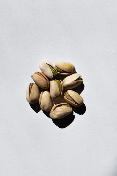 top view of pile with cracked green and salty pistachios on white background  - Photo, Image