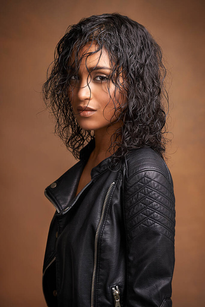 Leather and style. Studio shot of an attractive young woman in a leather jacket against a brown background. - Photo, Image