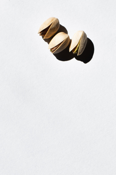 top view of cracked and organic pistachio nuts on white - Zdjęcie, obraz