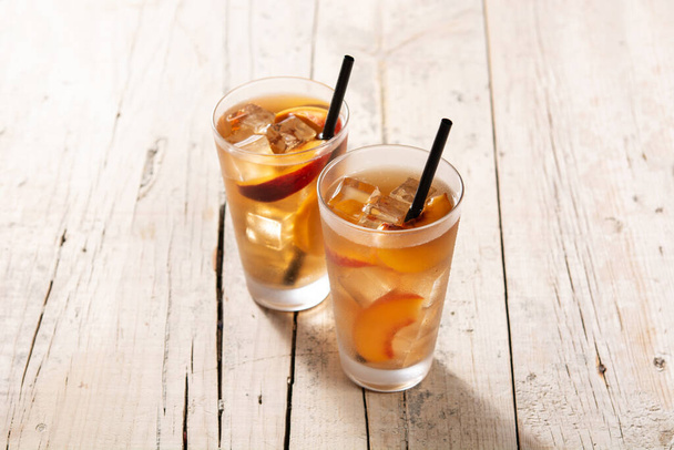 Glass of peach tea with ice cubes on wooden table - Foto, Imagem