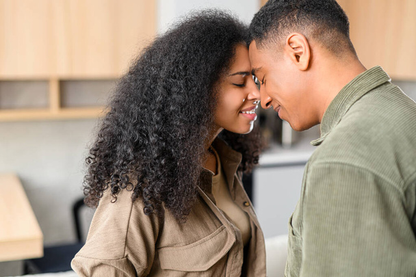 Lovely multiracial couple touching with foreheads in cozy modern kitchen at home. Smiling guy is bonding to his charming girl - Fotografie, Obrázek