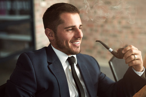 Volhardend en succesvol. Shot van een stijlvolle zakenman roken van een pijp in het kantoor. - Foto, afbeelding