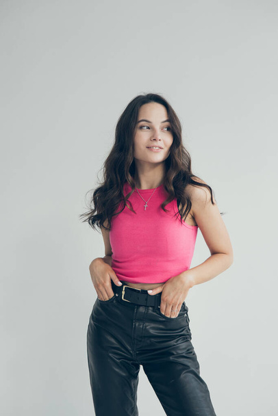 Young slim brunette woman in pants and shirt smiles and poses against grey background. Grey background isolated image. - Фото, изображение