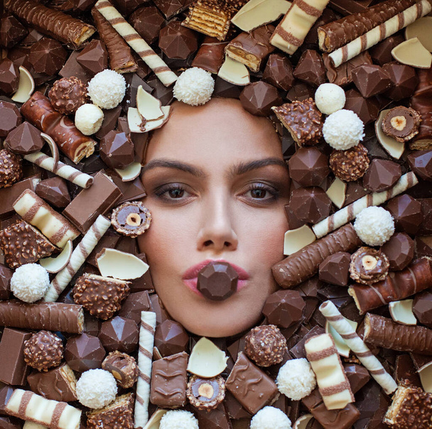 Beauty woman fashion art portrait over dark brown chocolate background. Young woman with beautiful skin and chocolate candy in her mouth. - Valokuva, kuva