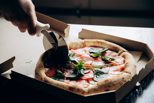 Deliciosa y jugosa pizza italiana con salchicha se corta con un cuchillo - Foto, Imagen