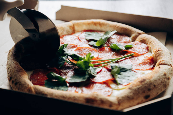 Deliciosa y jugosa pizza italiana con salchicha se corta con un cuchillo - Foto, imagen
