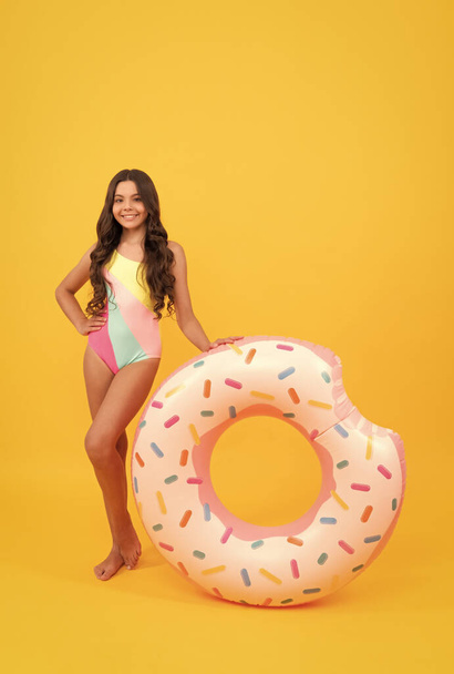 пляжна дівчина-підліток у купальнику з пончиком надувний кільце на жовтому фоні, пляжний аксесуар
. - Фото, зображення