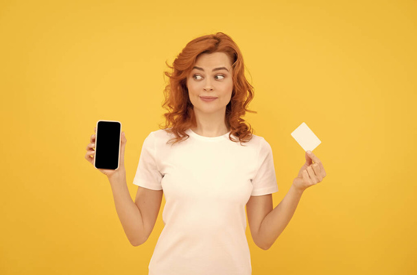 έκπληκτη γυναίκα που δείχνει πιστωτική ή χρεωστική κάρτα και smartphone για να κάνει online αγορές, σε απευθείας σύνδεση επιχείρηση. - Φωτογραφία, εικόνα