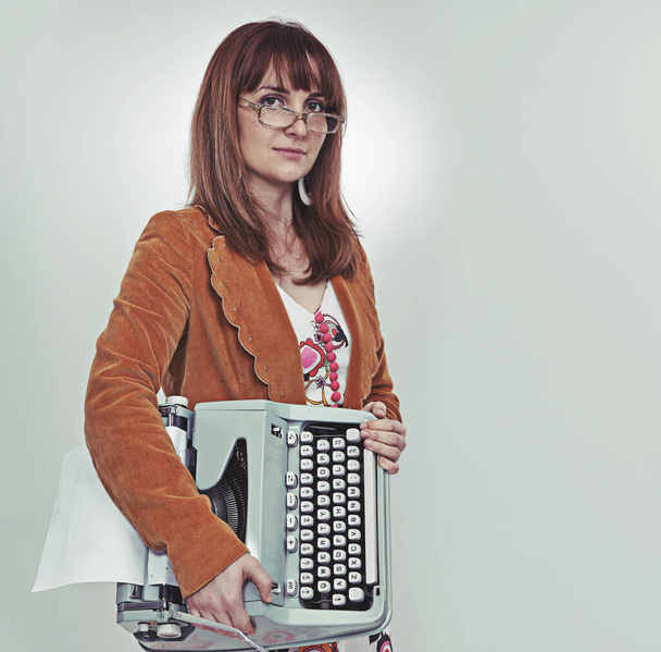 You want her as your secretary. Studio shot of a bookish young woman in retro clothing hugging her typewriter. - Foto, Imagem
