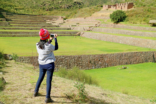 Female visitor taking photos of the ancient stepped agricultural terraces of Tipon, the Sacred valley of the Inca , Cusco region, Peru - 写真・画像