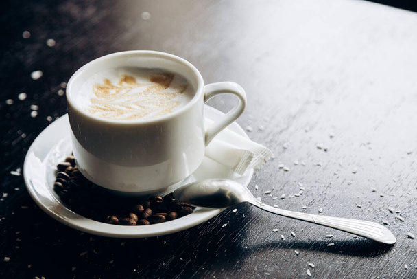 Λευκό φλιτζάνι ζεστό νόστιμο καφέ στέκεται στο τραπέζι με κόκκους καφέ - Φωτογραφία, εικόνα