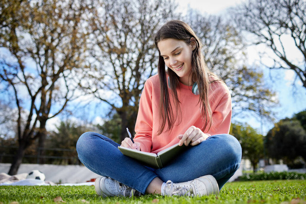 Ya tengo algunas ideas para mi tarea. Fotografía de una estudiante escribiendo en su cuaderno mientras estaba sentada afuera. - Foto, imagen