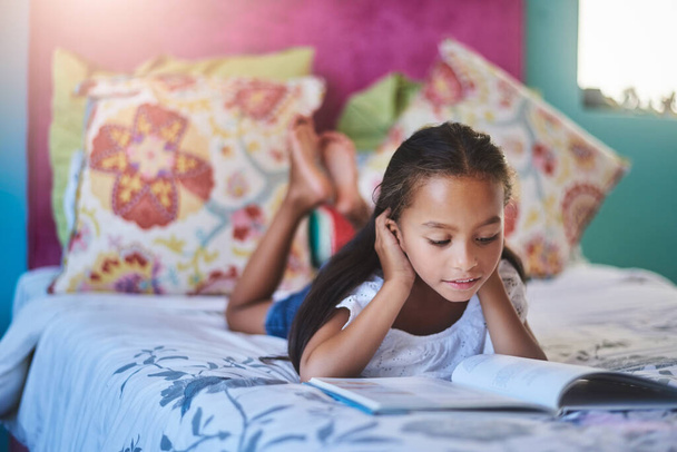 Se pierde en cada página. Foto de una adorable niña leyendo un libro en casa. - Foto, imagen