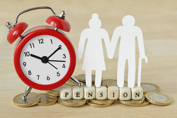La palabra Pensión escrita con bloques de madera, papel pareja de ancianos y reloj despertador en monedas - Concepto de tiempo de pensión - Foto, imagen
