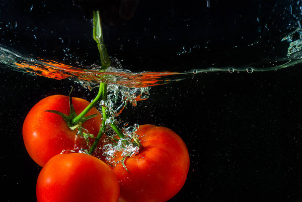 Fresh red tomato falling into water with water splash and air bubbles isolated on black background. - Photo, Image