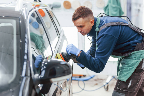 Male worker in uniform polishing new modern car. Conception of service. - Фото, зображення