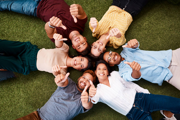 We hope lots of good comes your way. Portrait of a group of young creatives showing thumbs up while lying down in a huddle together. - Valokuva, kuva