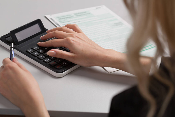 primer plano de una mujer que hace una declaración de impuestos utilizando una calculadora - Foto, Imagen