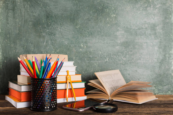 Stapel von Büchern und Schreibwaren auf dem Hintergrund der Schultafel. Bildung und zurück zum Schulkonzept. - Foto, Bild