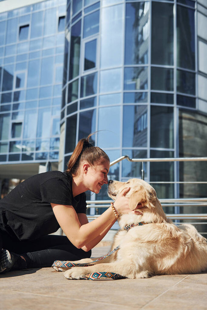 Young positive woman have fun with her dog when have a walk outdoors near business building. - Fotoğraf, Görsel