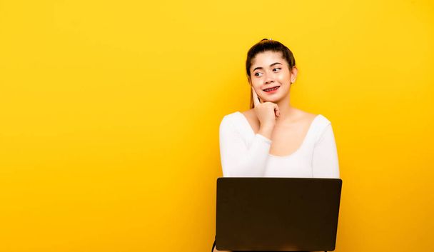 Got an idea, an amazing close-up of an attractive Asian woman. laptop woman looking up empty space deep thinking creative isolated yellow background - Photo, Image