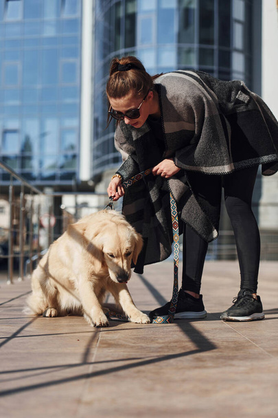 Young positive woman have fun with her dog when have a walk outdoors near business building. - Foto, Imagen
