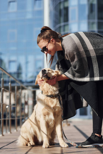 Young positive woman have fun with her dog when have a walk outdoors near business building. - 写真・画像
