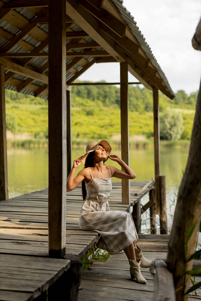 Mujer joven relajándose en el muelle de madera en el lago tranquilo en un día caluroso de verano - Foto, imagen