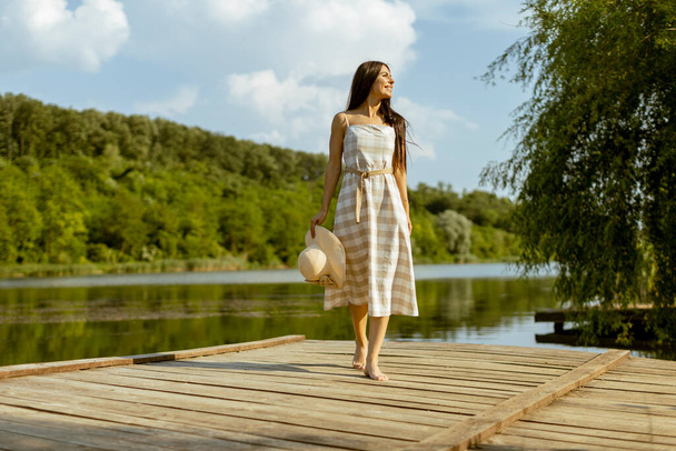 Young woman walking on the wooden pier at the calm lake on a hot summer day - Foto, Imagem