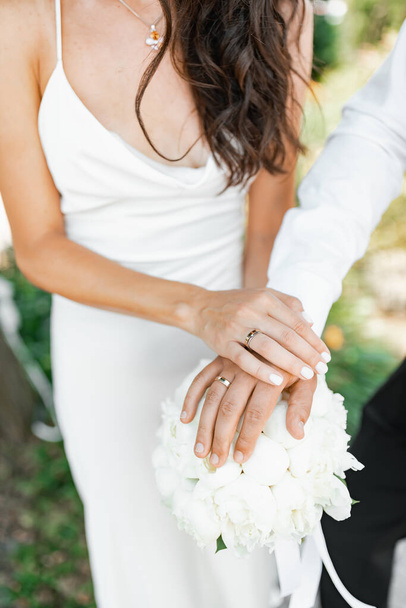 Nur Hände aus nächster Nähe. Multikulturelles glückliches Paar im Hochzeitsoutfit. Die Braut hat einen weißen Strauß. Botanischer Garten - Foto, Bild